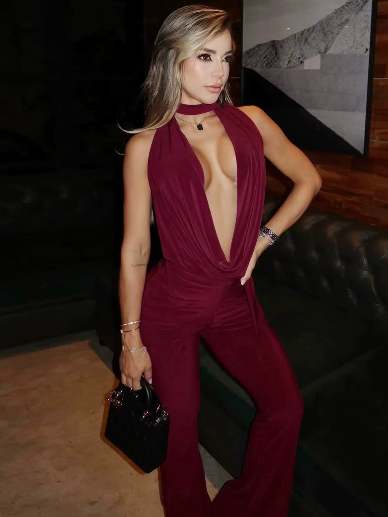 Model wearing burgundy deep-plunge jumpsuit with scarf neckline in nightclub setting