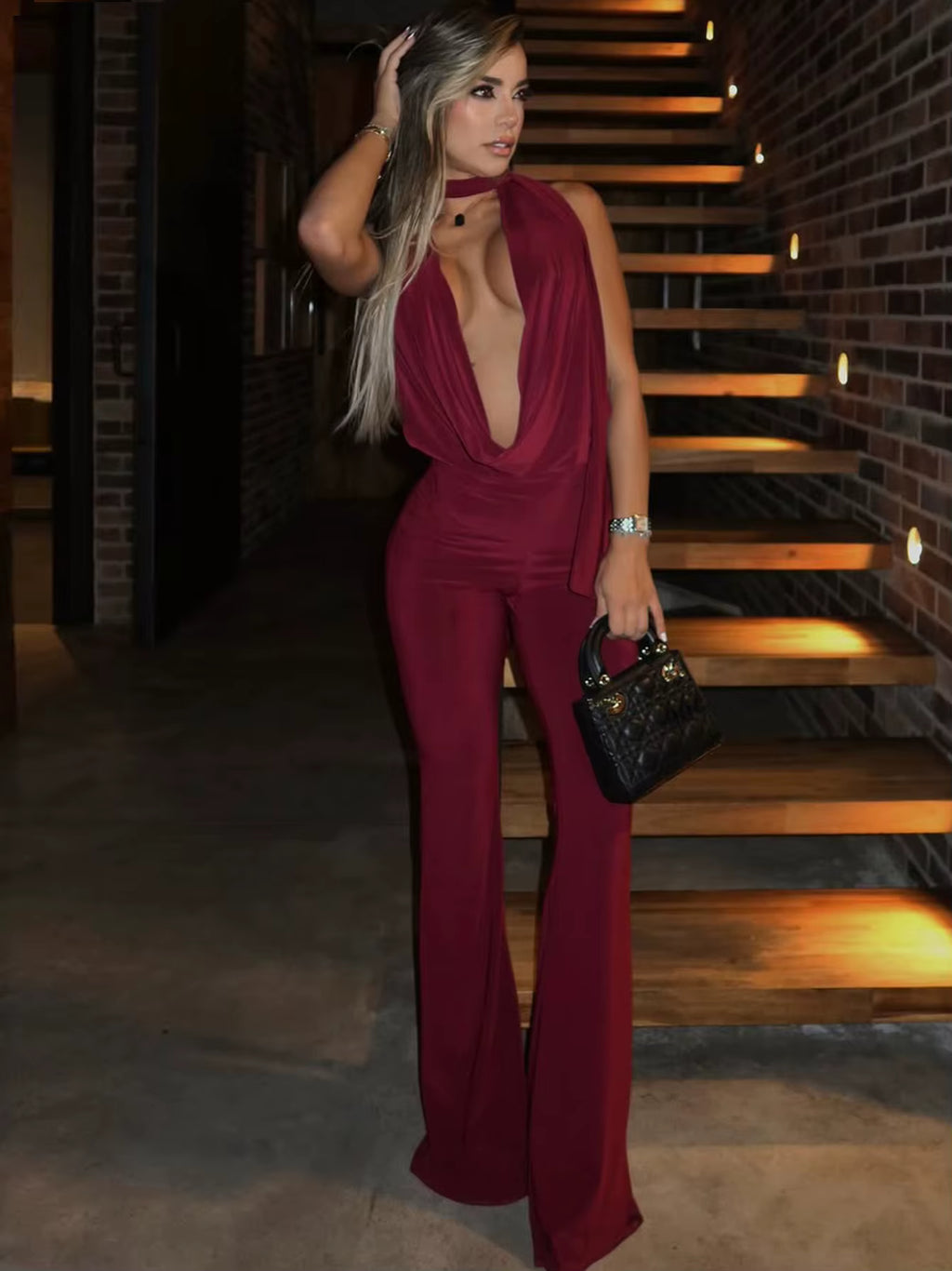 Model walking in burgundy plunge jumpsuit with open back and fitted legs