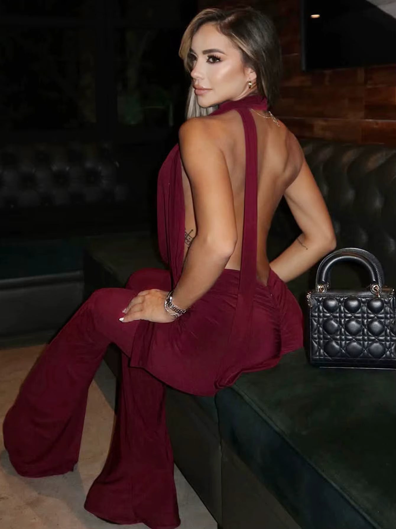 Model sitting in burgundy backless jumpsuit showing low open back